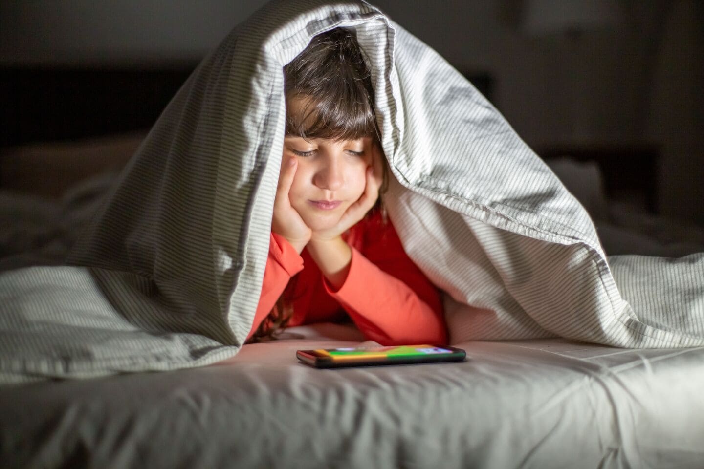 A parent comforts a child at bedtime in a dim, cozy bedroom.